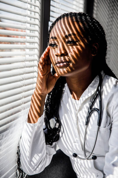 istock Female scientist standing by the window, blind shades playing on her face while she takes a break from work 1460498534
