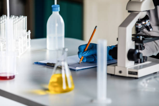 Cut out shot of unrecognizable female scientist analying samples under the microscope and writing her findings on the clipboard.