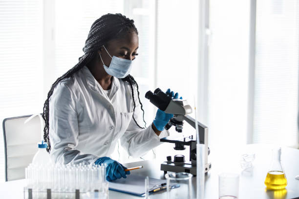istock Young female scientist analying samples under the microscope and writing her findings on the clipboard 1460498895