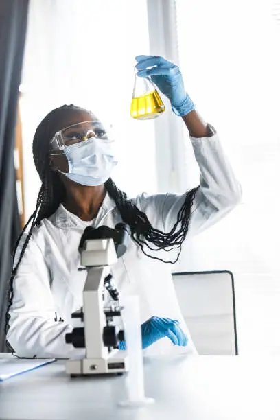 Photo of Laboratory technician in protective gear analyzing yellow liquid for research