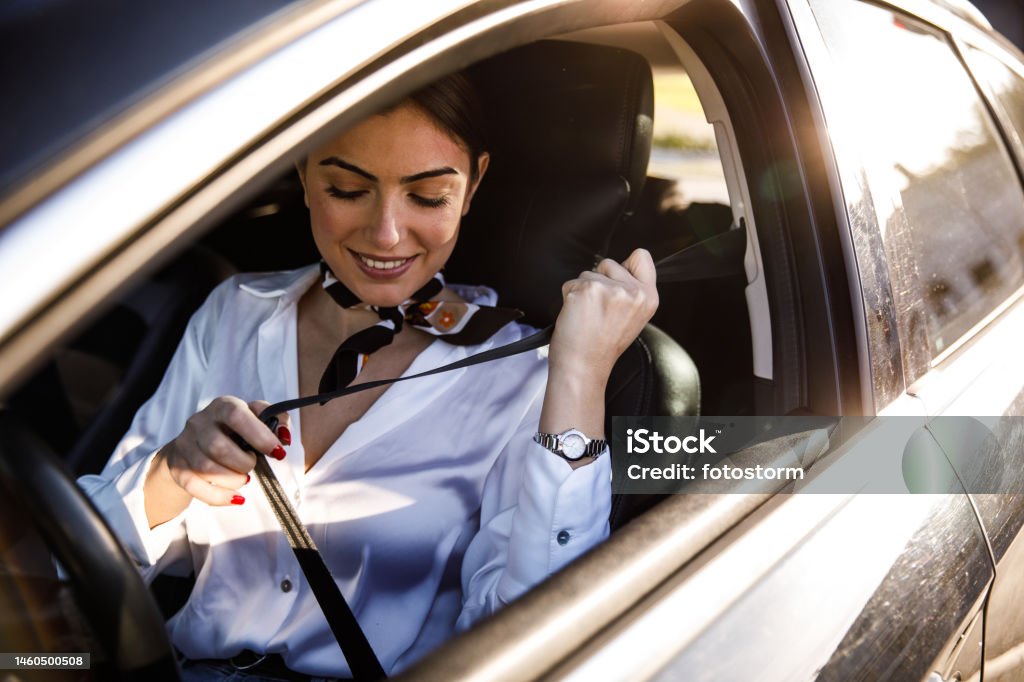 Smiling young woman sitting in her car and fastening a seat belt before driving Copy space shot of charming young woman sitting in driver's seat of her car and fastening a seat belt before driving. 20-24 Years Stock Photo