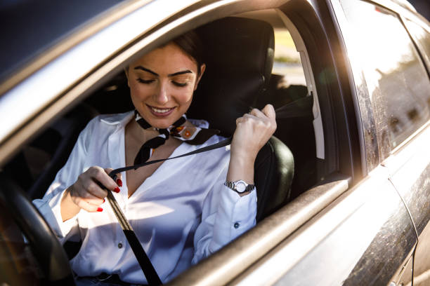 Smiling young woman sitting in her car and fastening a seat belt before driving stock photo