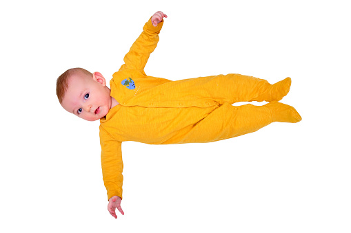 Infant baby lies on a play mat in yellow pajamas, top view, isolated on a white background. Toddler on the white floor full length, copy space. Kid aged six months
