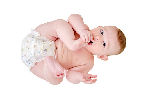 A happy infant baby with teething teeth in a diaper pulls his hand into his mouth, isolated on a white background. Funny child in a crib. Kid aged six months