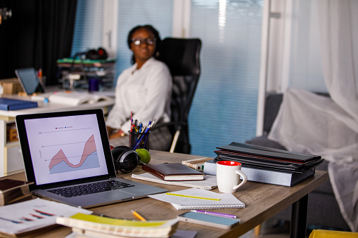 Selective focus shot of a messy desk with a graph on laptop screen in a co-working office space. Part of a series.