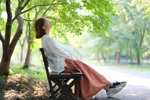 young woman sitting bench in park under green tree on sunny day