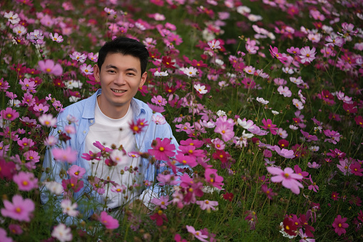 portrait of smile handsome Asian young man in pink red galsang flowers field, looking at camera
