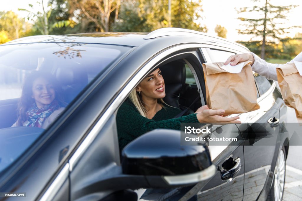 Young woman sitting in her car, receiving her takeaway food at the drive through Cut out shot of smiling young woman sitting in her car, receiving her takeaway food from the service person at the drive through. Fast Food Restaurant Stock Photo