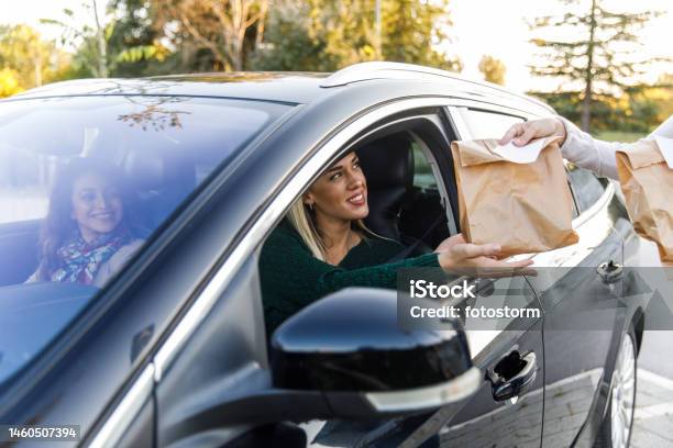 Young Woman Sitting In Her Car Receiving Her Takeaway Food At The Drive Through Stock Photo - Download Image Now