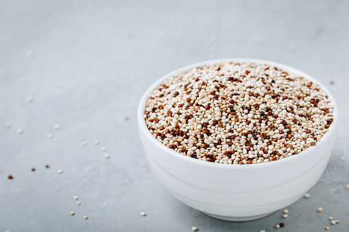 Quinoa. Red white brown quinoa seeds in bowl. Mixed organic raw quinoa seeds on gray stone background.