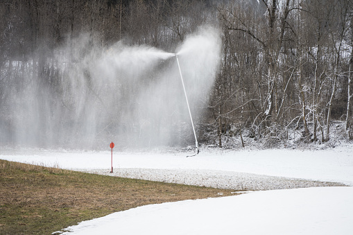 Snow cannon lance gun to produce artificial snow in ski resorts and on the slopes in front of brownish green grass in winter with little snow as a concept for climate change and global warming