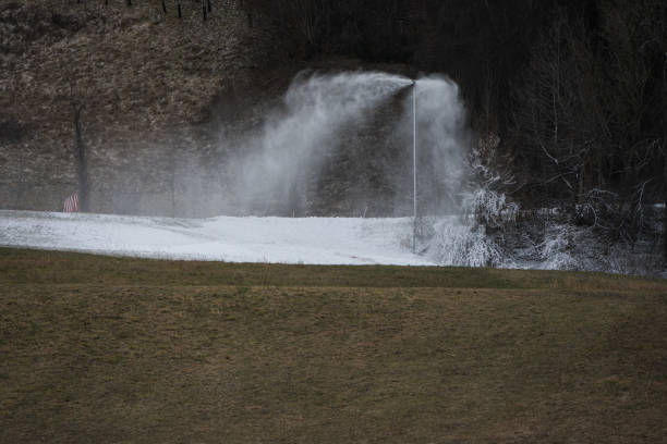 Snow lance cannon producing artificial snow on slopes and in ski resorts with green brownish grass in foreground during winter with missing snow as a concept for global warming and climate change