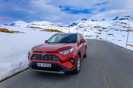 Toyota SUV on the road in front of snowcapped mountain ranges near Krossbu, Jotunheimen National Park, Norway