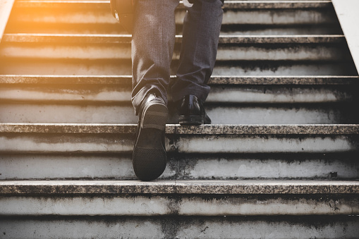 Step to success concept Sucessful business man walking up stairs Businessman with bags in his hands walking stairs going to office in the morning Elegant man in suit taking steps with sunlgiht