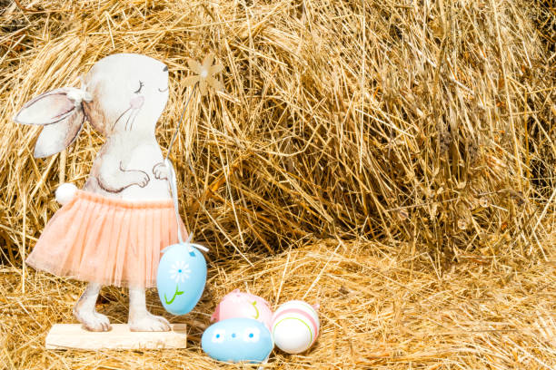 A wooden rabbit in a cute skirt on a hay background with painted Easter eggs. Easter, a postcard with a place for text