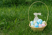 A wicker basket with Easter eggs and a wooden hare on the green grass, lawn. Easter card with a place for text