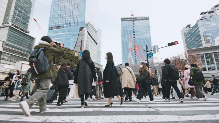 Crowd people walk cross road at Shibuya scramble crossing, low angle view slow motion. Tokyo tourist attraction landmark, traffic transportation, Japan tourism, Asia transport, Asian city life concept