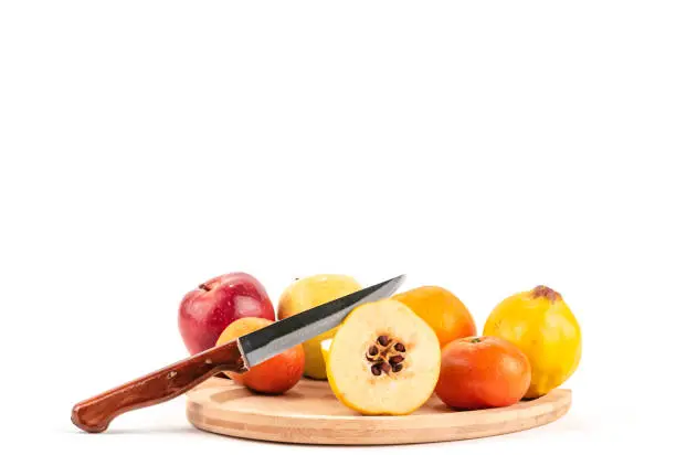 Photo of Half cutted quince and fruits on a wooden plate with knife white background.