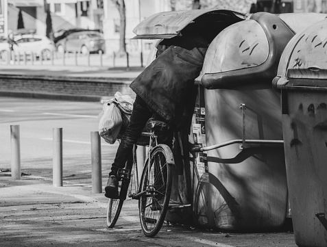 Skopje, Macedonia - 01 22 2023: homeless man on a bicycle searching for goods in a public garbage container