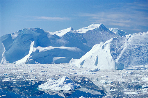 On a rare clear day, snow covered mountains rise out of the waters of the Antarctic Peninsula as an iceberg floats by the scene.