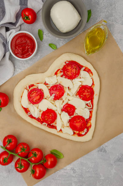 istock Pizza Margherita shaped heart with cherry tomatoes, mozzarella and basil on a gray concrete background. Food concept for Valentine's Day. Copy space. 1460531122