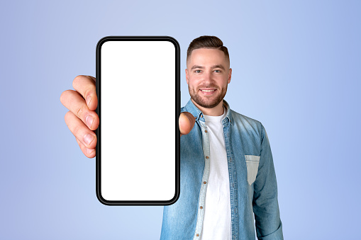 Happy man portrait showing a big smartphone mock up empty screen, blue background. Concept of social media, mobile app and online communication