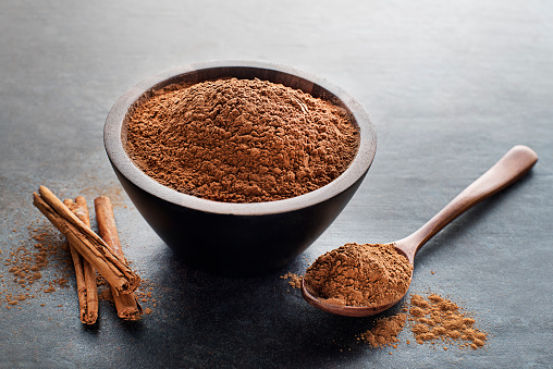 Aromatic cinnamon sticks with cup and spoon with powder on grey background close up