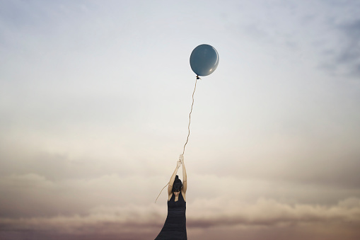 woman clings to a balloon flying in the sky, abstract concept