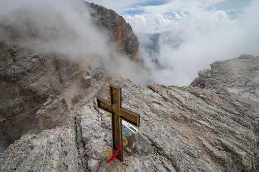 View obscured by clouds from the top of the Cima di Mezzo mountain (3154 m) with a beautiful cross on the top. Dolomites, Italy
