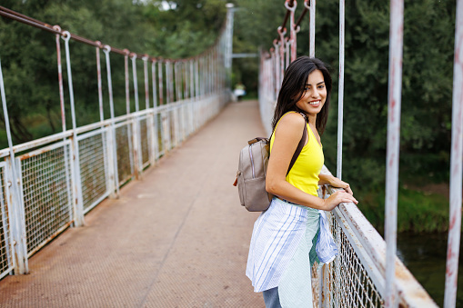 Beautiful young woman standing on footbridge and enjoying the view on river
