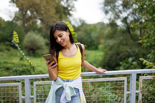 Beautiful young woman typing on mobile phone while standing on footbridge in nature
