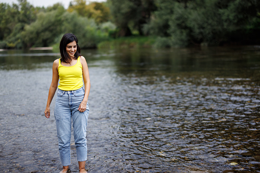 Young woman in jeans walking into river on sunny day