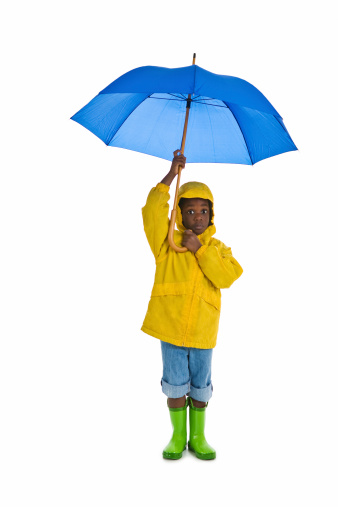 A young African American boy wearing a yellow rain slicker and carrying a blue umbrella. Isolated on a white background.