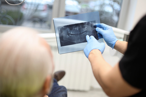 Senior man at a dentist's office, looking at a medical dental scan. Unrecognizable Caucasian males.