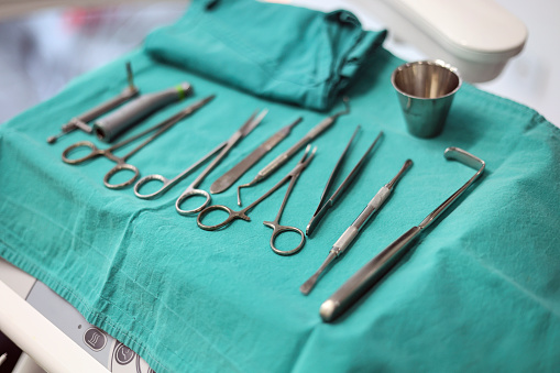 Close-up of various pieces of sterilized surgical equipment laid out on green cloth covering medical tray and ready for medical procedure.