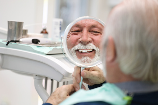 Senior man looking in a mirror at a dentist's office. About 65 years old, Caucasian male.