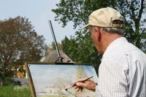 Senior male artist painting by a river.