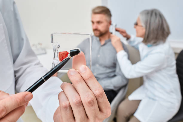 Hearing aid specialist doing ear examination and recommended Completely-in-Canal hearing aid to patient . Choosing between In-The-Canal and In-The-Ear hearing aids Hearing aid specialist doing ear examination and recommended Completely-in-Canal hearing aid to patient . Choosing between In-The-Canal and In-The-Ear hearing aids Doctor showing hearing aid stock photo stock pictures, royalty-free photos & images