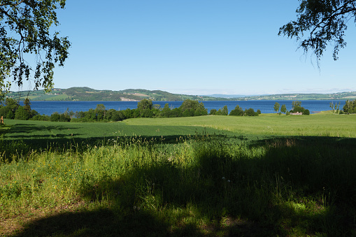 Mjøsa near Hamar in spring. In the foreground trees, meadows and fields. Mjøsa is Norway's largest lake. Seen on the pilgrimage route St. Olavsweg, Gudbrandsdalsleden from Oslo to Trondheim.