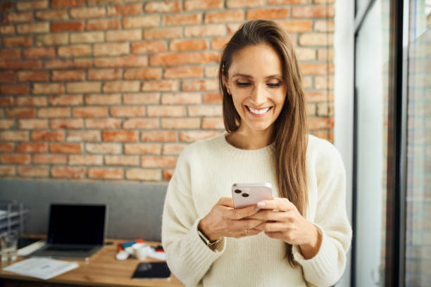Smiling female entrepreneur at small office using smartphone stock photo