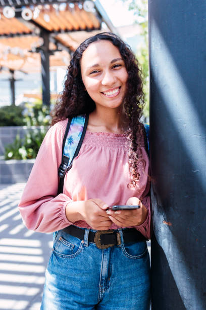 istock Latin university student woman leaning on a pillar, smiling and using her mobile sitting outside the campus in free time 1460548743