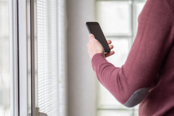 istock Man standing next to windows at home and using smartphone 1460548776