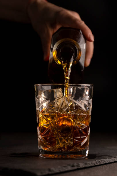 bartender pours whiskey or rum into a glass stock photo