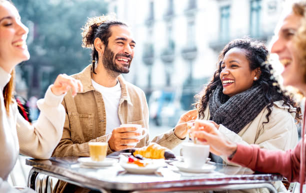 Young couples drinking cappuccino at coffee bar patio - Friends talking and having fun together at sidewalk cafeteria - Life style concept with young men and women at cafe dehor - Bright vivid filter stock photo