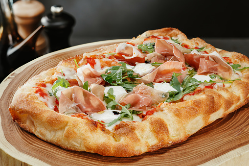 Crispy gourmet Pizza with cheese, ham, sweet red pepper and arugula leaves on wooden kitchen boards. Shallow depth of field