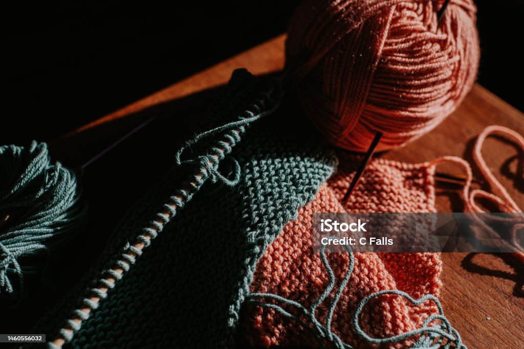 Close-up of two balls of yarn beside knitting A pink ball of yarn and a turquoise ball of yarn beside knitting needles and knitting. Knitting Stock Photo