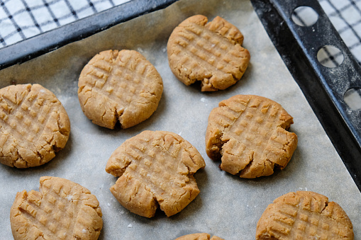 Close up of baked american peanut butter cookies on a baking sheet lined with baking paper laying on a checkered napkin