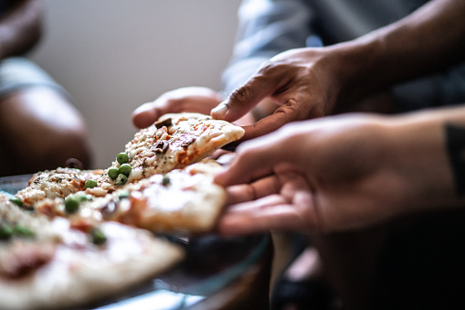 Close-up of friends picking slices of pizza at home