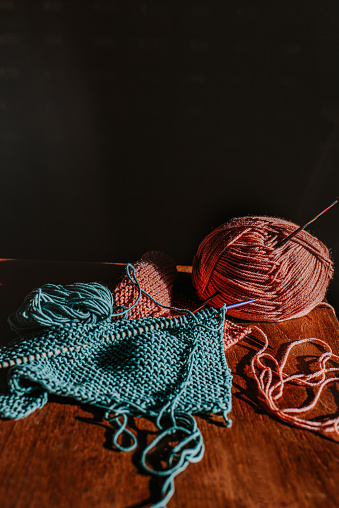A pink ball of yarn and a turquoise ball of yarn beside knitting needles and knitting.