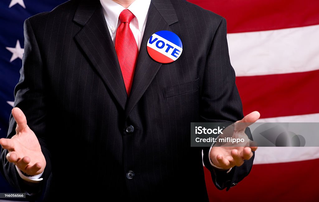 An American politician campaigning  A politician or business man standing in front of an American flag stumping or pleading with people to vote, exercise privilege as an American citizen Adult Stock Photo
